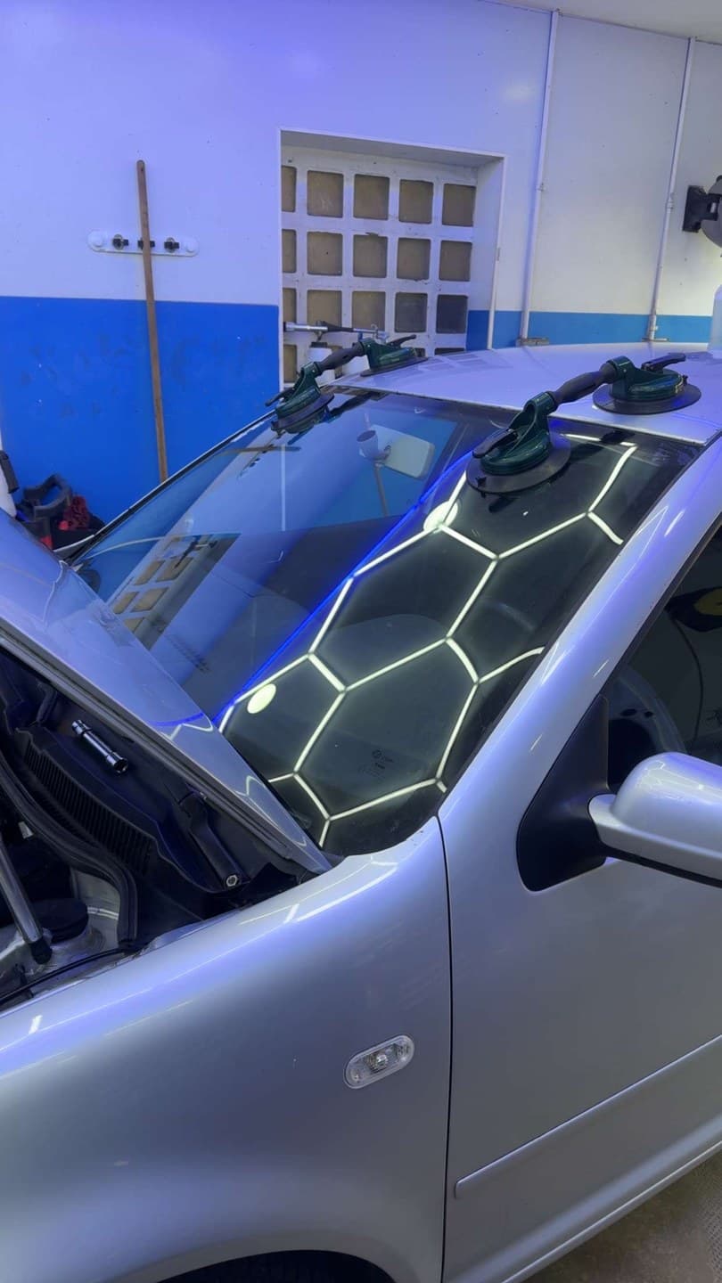 Volkswagen Golf IV grise en atelier, pare-brise manipulé à la ventouse pendant la pose