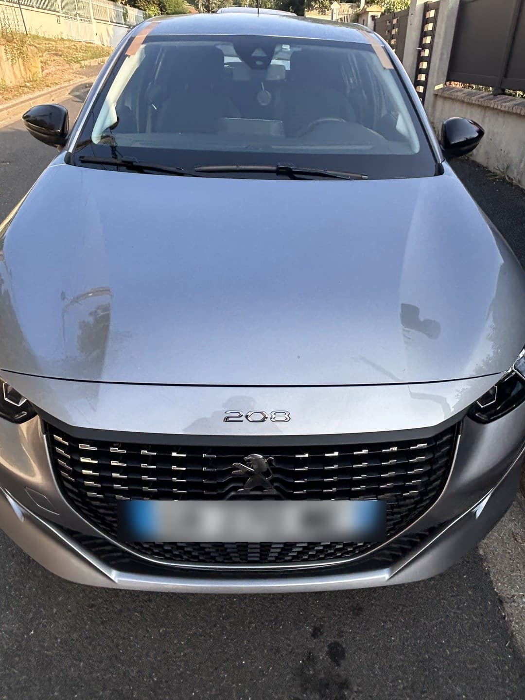 Peugeot 208 II grise, pare-brise neuf posé et maintenu par les adhésifs le temps de la prise de la colle