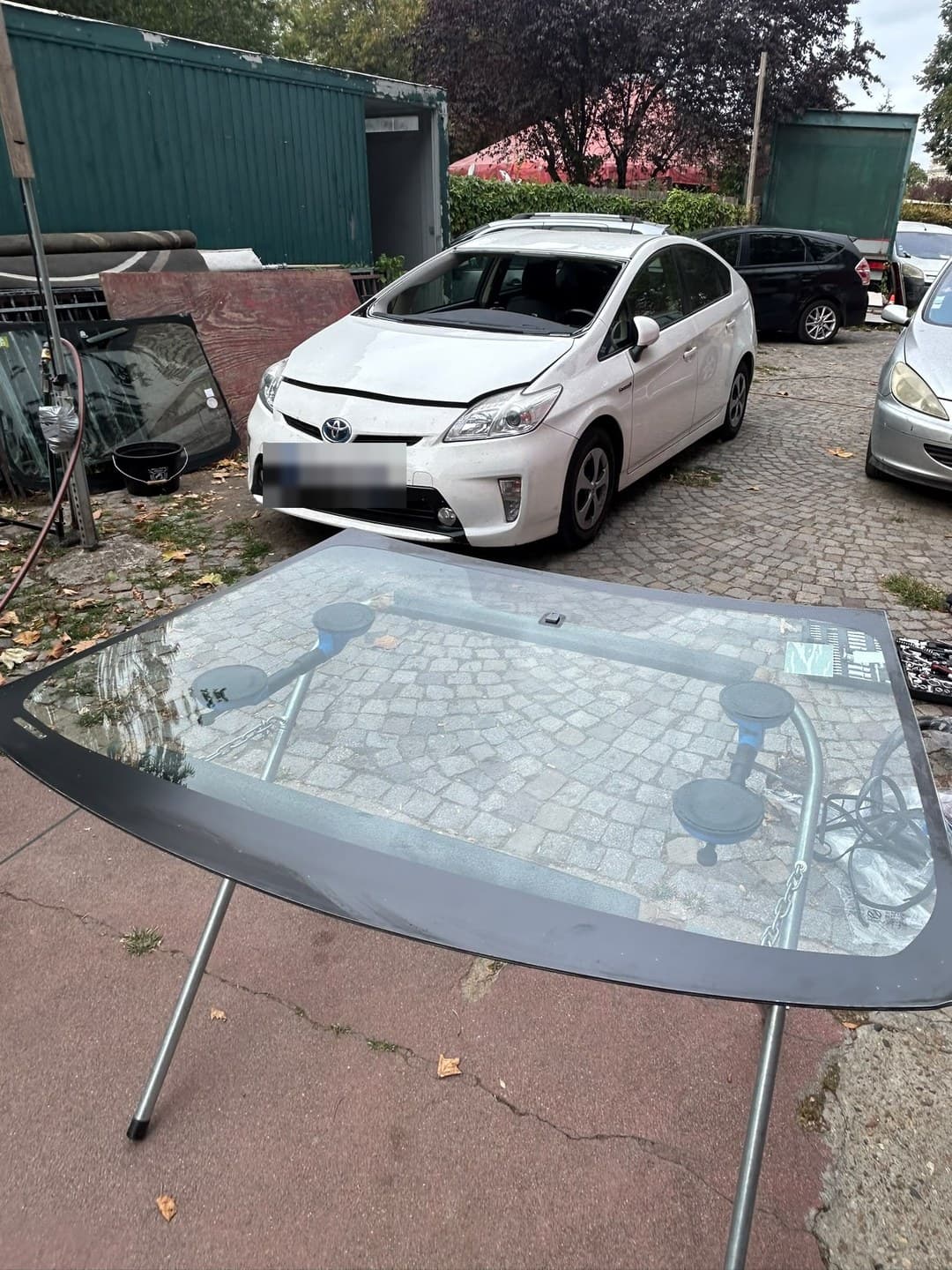 Toyota Prius blanche, pare-brise neuf sur tréteaux, ventouses en place, juste avant la pose