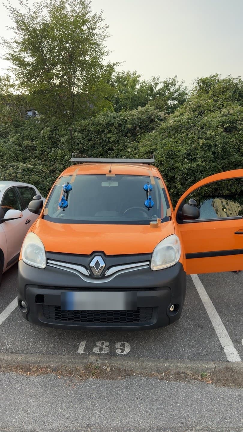 Renault Kangoo orange sur sa place de parking, ventouses posées sur le pare-brise neuf