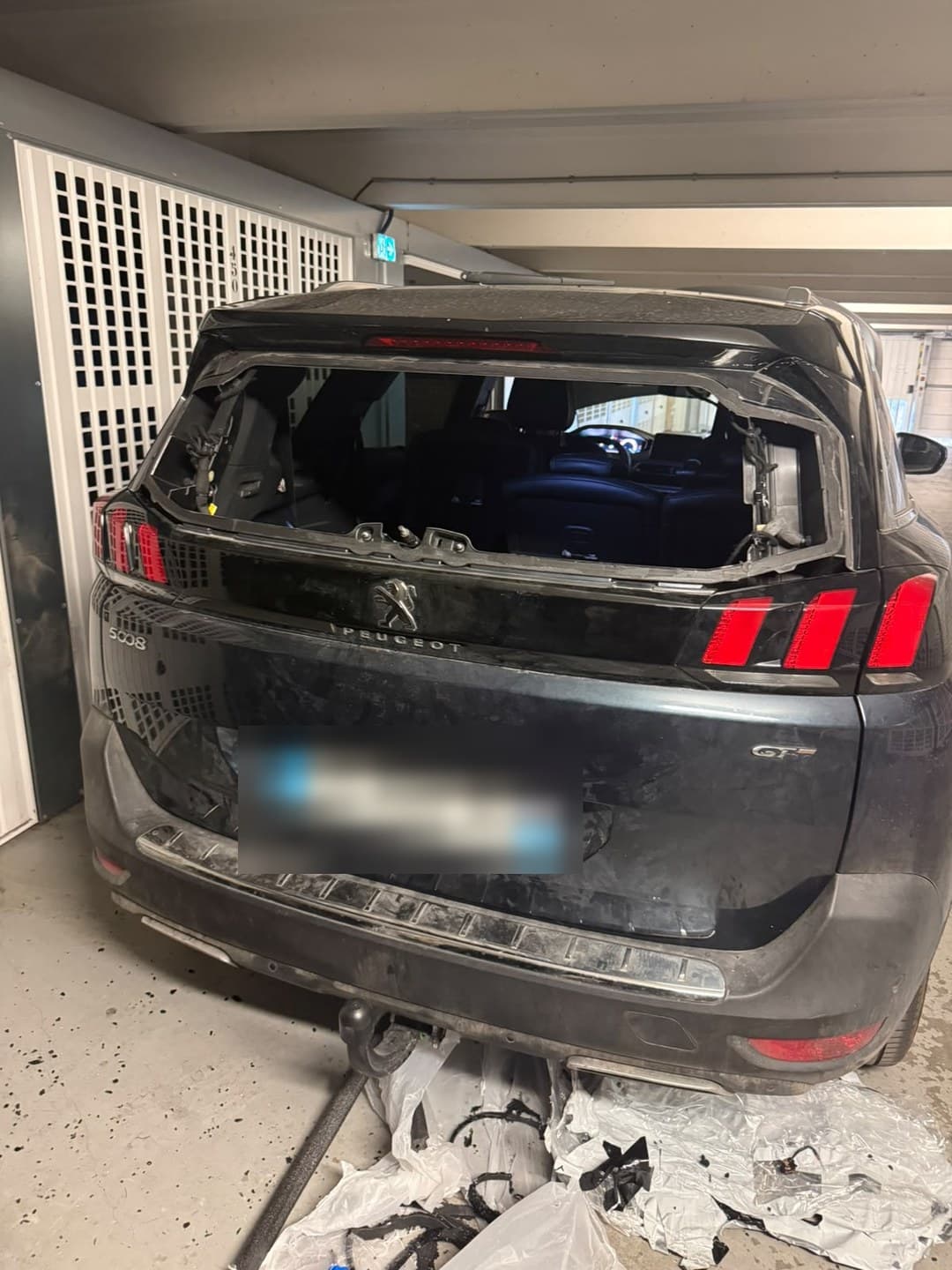 Peugeot 5008 II en parking souterrain, lunette arrière brisée : le hayon est ouvert au vent, les débris au sol